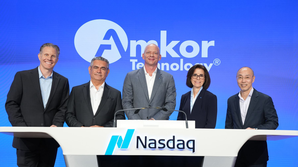 Five Amkor Technology leaders standing behind a Nasdaq podium with company branding on a blue background during Investor Day.