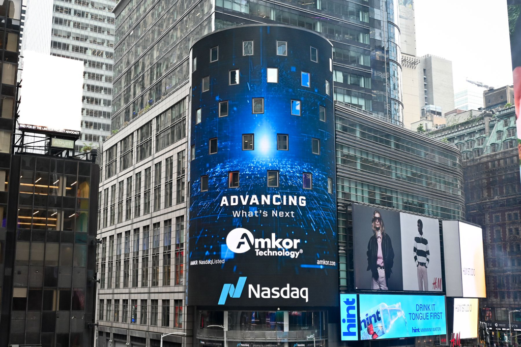 Amkor Technology displayed on a large digital billboard at the Nasdaq building in Times Square, featuring the message “Advancing What’s Next” with surrounding city skyscrapers.
