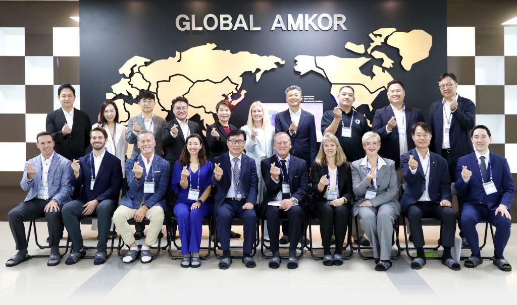 Arizona and Amkor representatives gather for a group photo in front of a Global Amkor display.